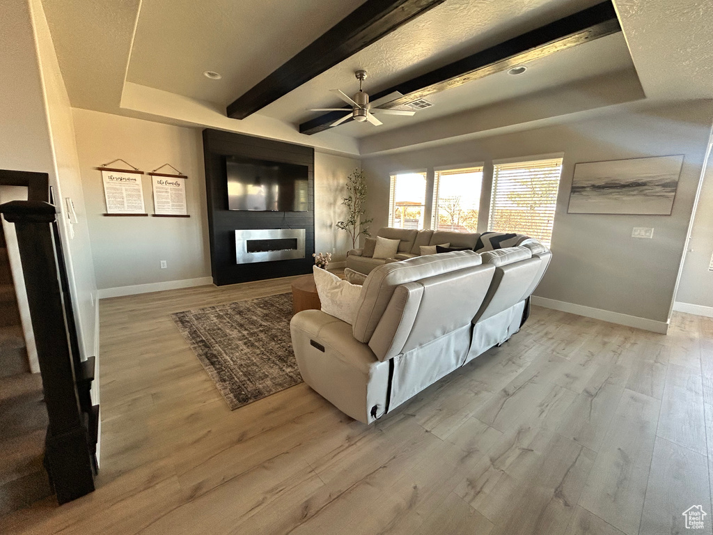 Living room with a tray ceiling, light hardwood / wood-style floors, a large fireplace, and beamed ceiling