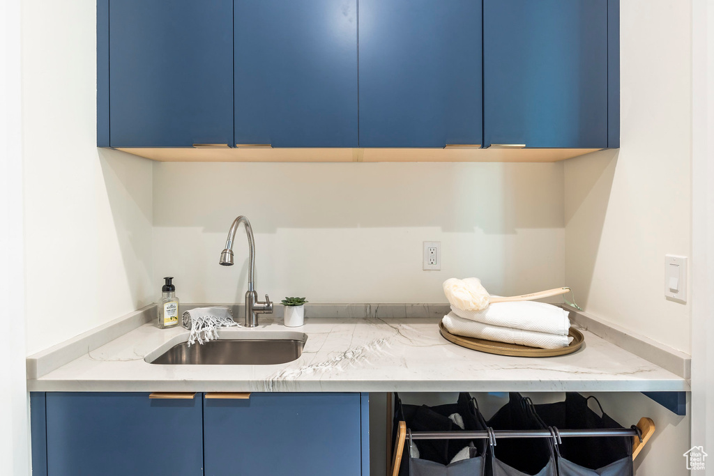 Kitchen featuring blue cabinetry, light stone countertops, and sink