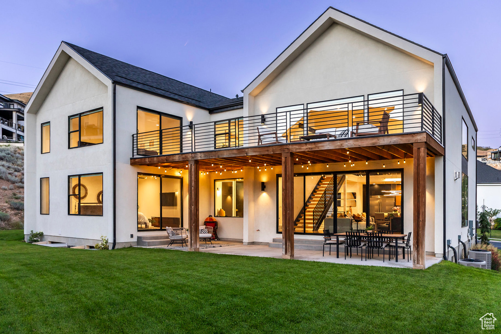 Back house at dusk featuring a yard, a balcony, and a patio