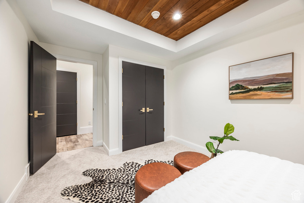 Bedroom featuring a raised ceiling, light carpet, a closet, and wooden ceiling