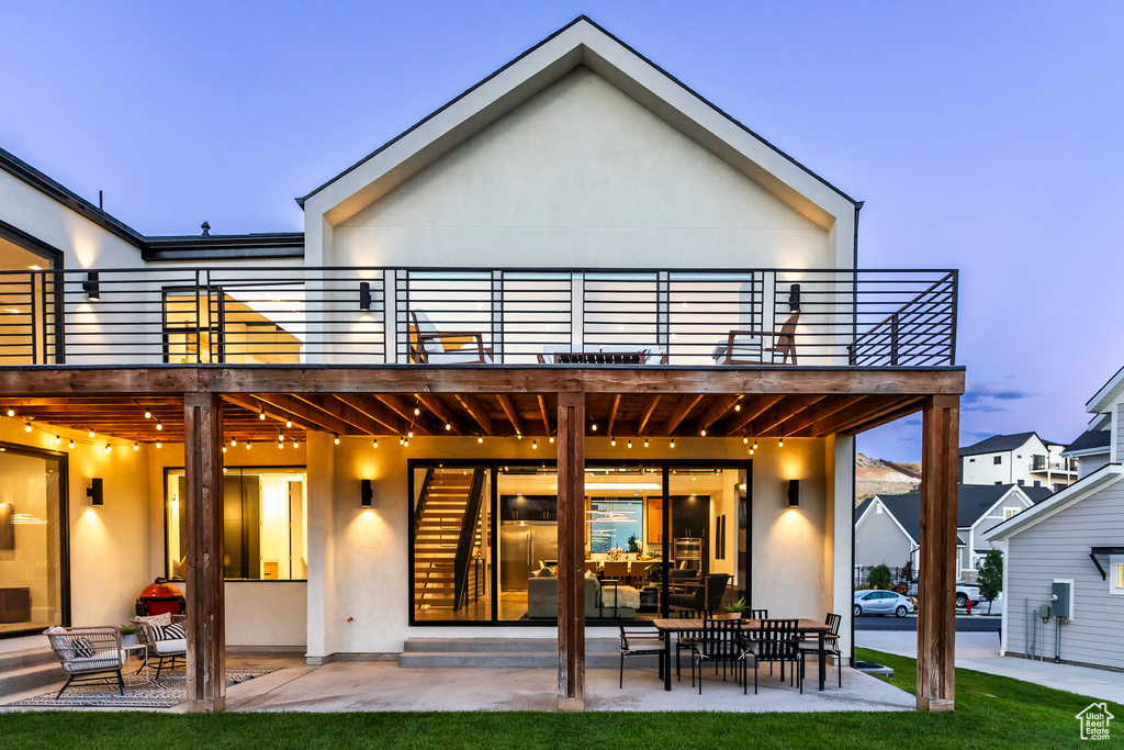 Back house at dusk featuring a balcony and a patio