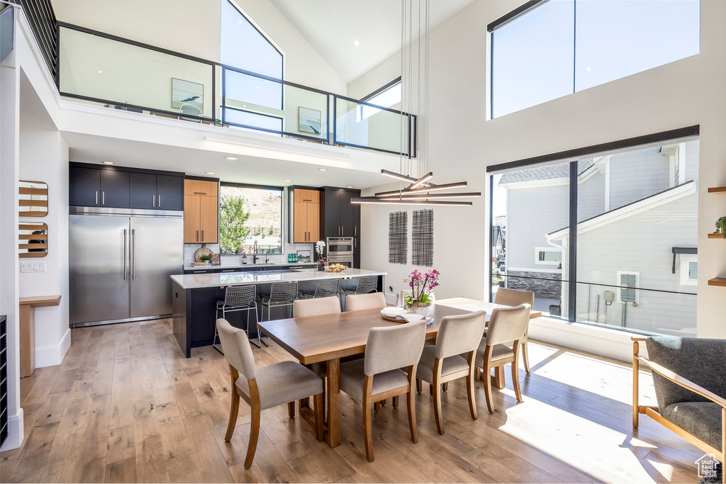 Dining room featuring a notable chandelier, light wood-type flooring, and a high ceiling
