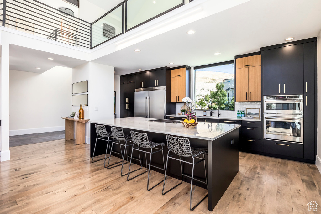 Kitchen with stainless steel appliances, light stone counters, a breakfast bar, a kitchen island, and light wood-type flooring