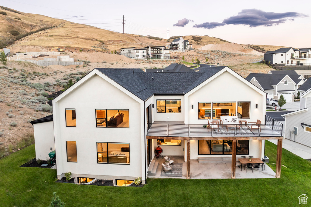 Back house at dusk featuring a lawn, a mountain view, a balcony, and a patio