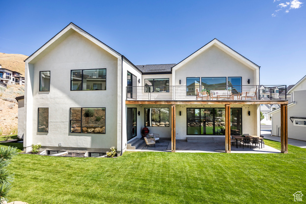 Rear view of house with a lawn, a balcony, and a patio