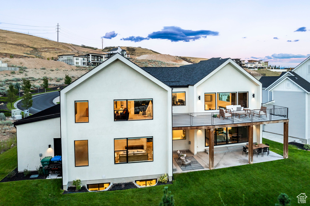 Back house at dusk with a yard, a balcony, and a patio