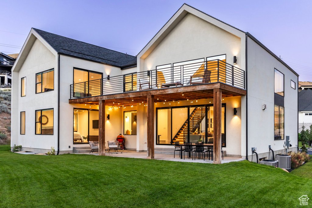 Back house at dusk with a lawn, a balcony, and a patio