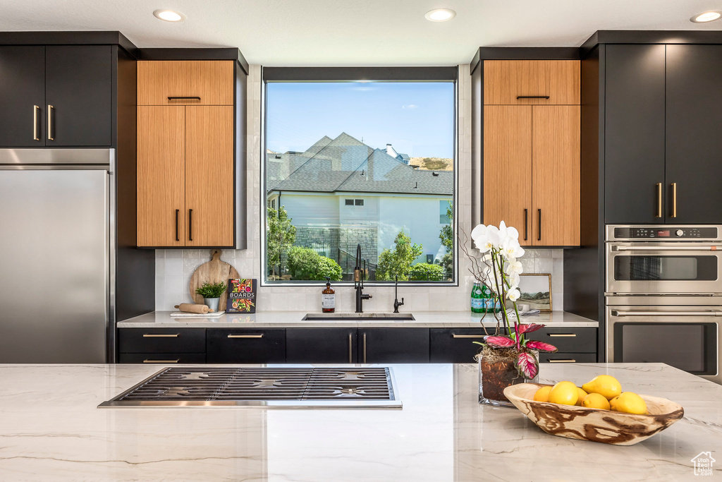 Kitchen featuring light stone counters, sink, appliances with stainless steel finishes, and tasteful backsplash