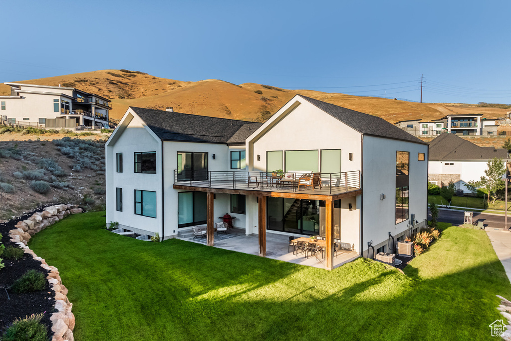 Back of house featuring a mountain view, a balcony, a yard, and a patio