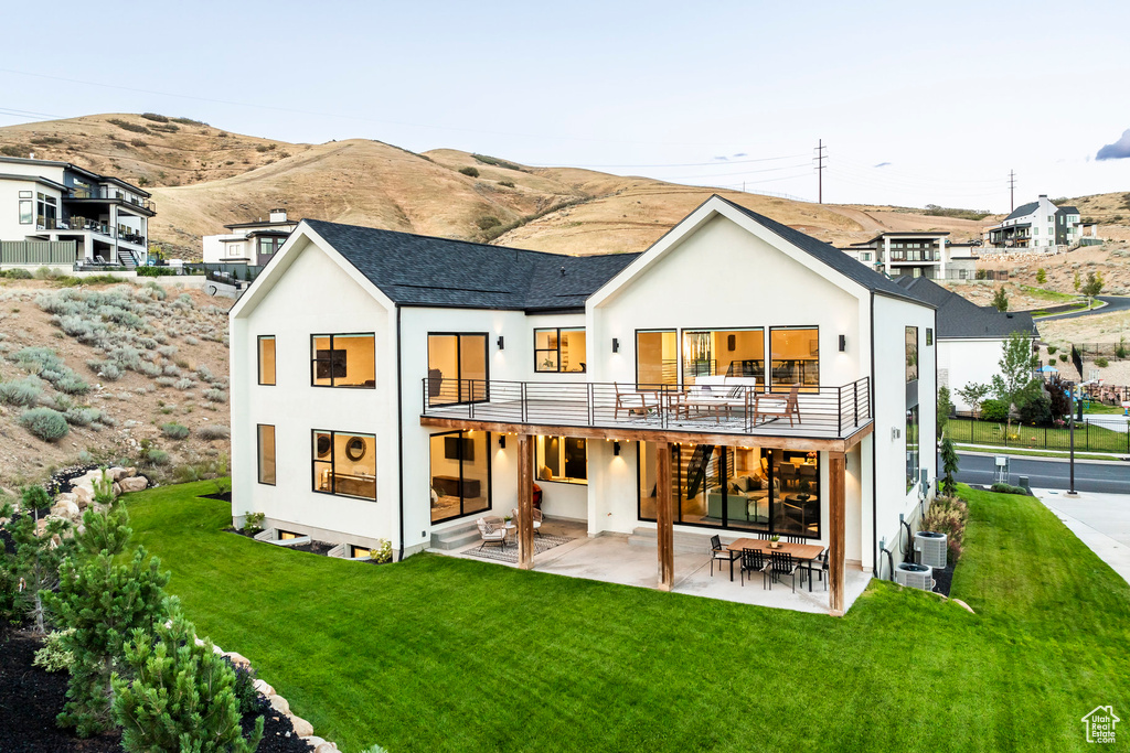 Rear view of house with a mountain view, central air condition unit, a balcony, a yard, and a patio area