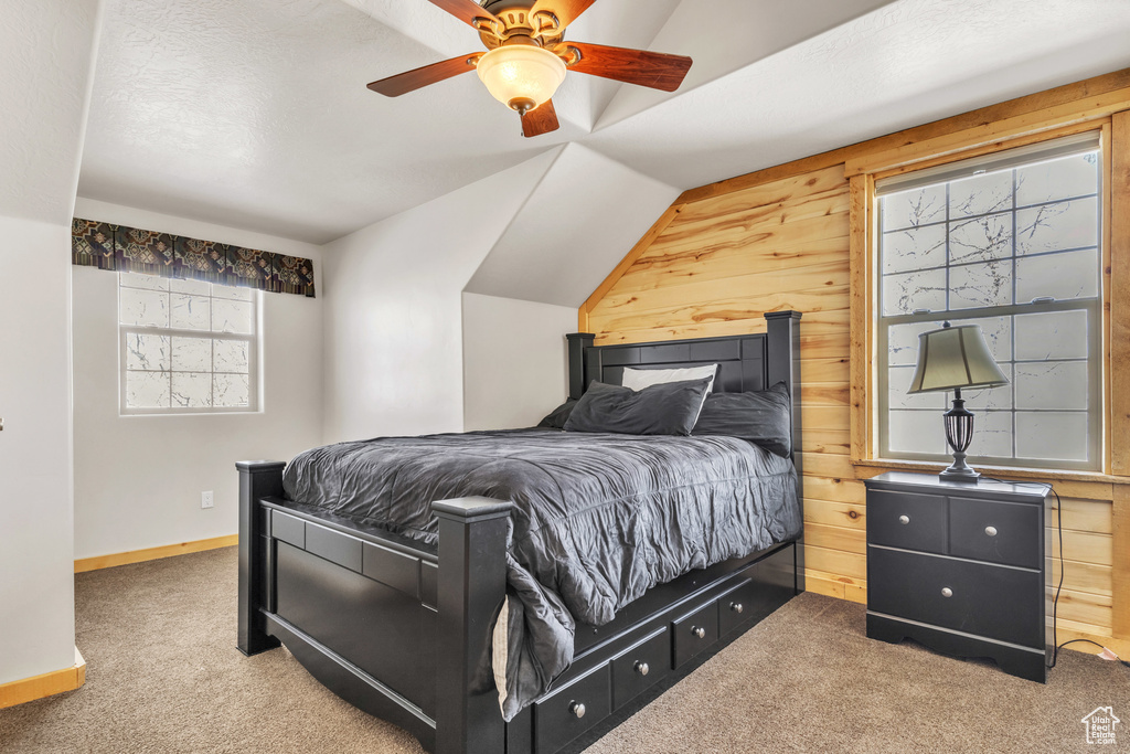 Carpeted bedroom with ceiling fan, lofted ceiling, and wooden walls