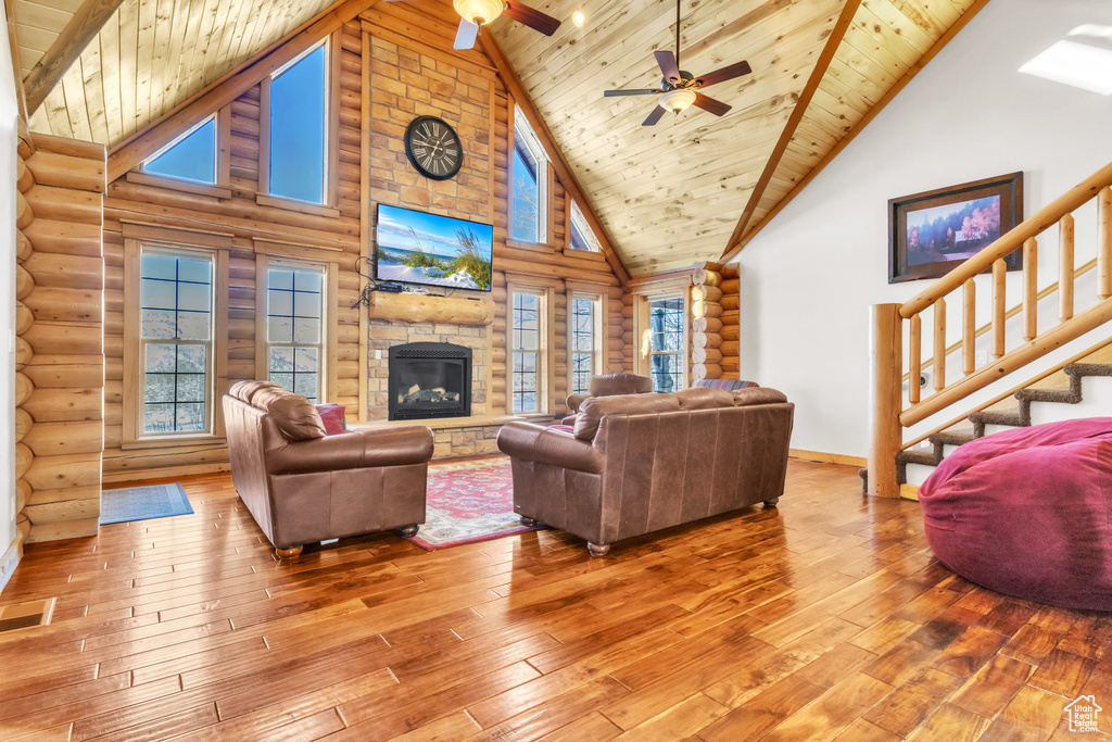 Living room with rustic walls, hardwood / wood-style floors, wood ceiling, and a stone fireplace