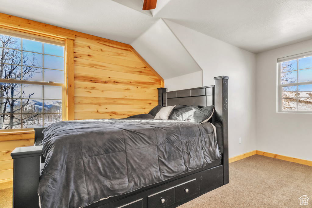 Bedroom with lofted ceiling, carpet floors, ceiling fan, and wooden walls
