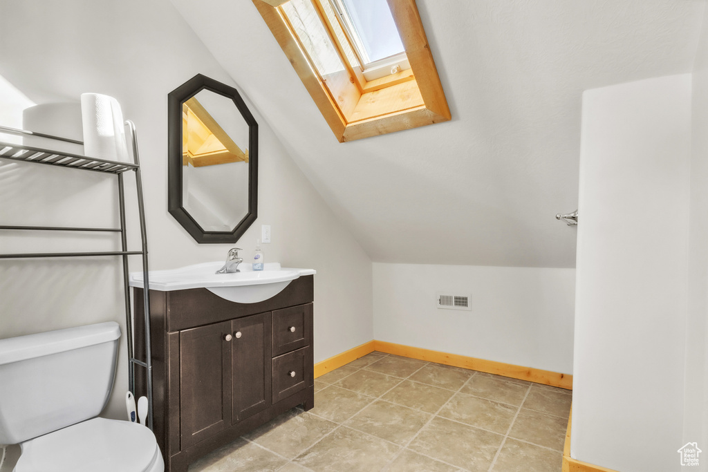 Bathroom with vaulted ceiling with skylight, vanity, and toilet