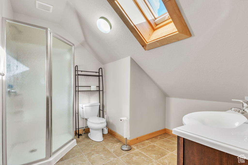 Bathroom featuring vaulted ceiling with skylight, vanity, toilet, and a shower with shower door