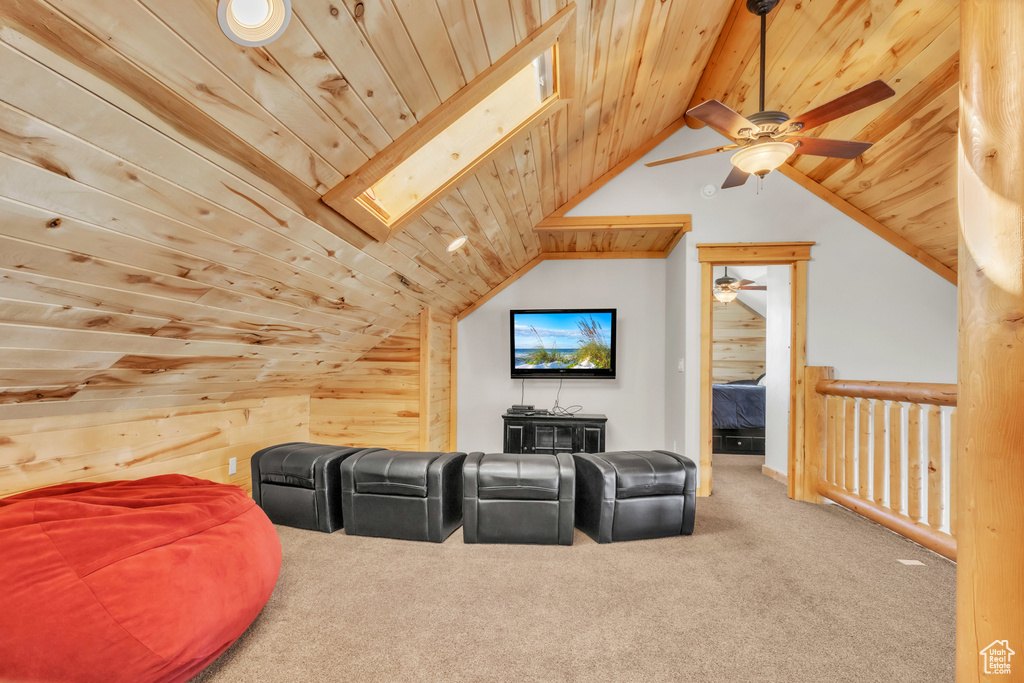 Home theater with carpet flooring, ceiling fan, wood walls, lofted ceiling with skylight, and wood ceiling