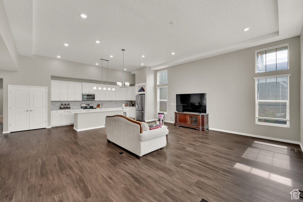 Living area with recessed lighting, dark wood finished floors, baseboards, a chandelier, and a high ceiling