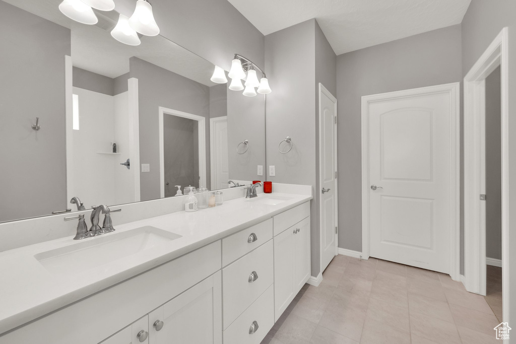 Bathroom with a chandelier, double vanity, tile patterned flooring, and baseboards