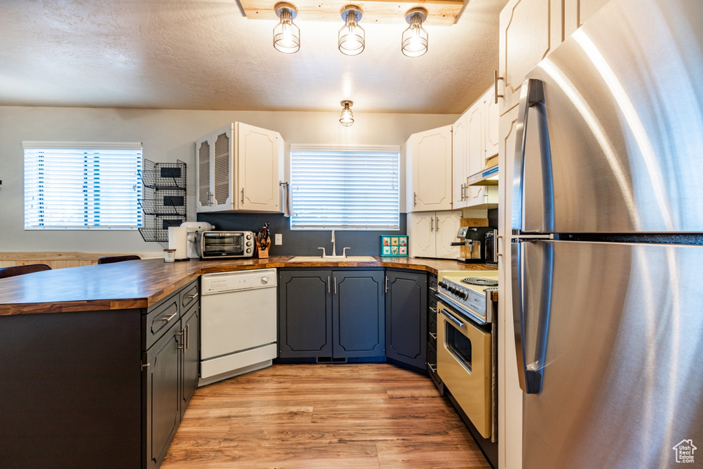 Kitchen with electric stove, dishwasher, white cabinets, butcher block countertops, and stainless steel refrigerator