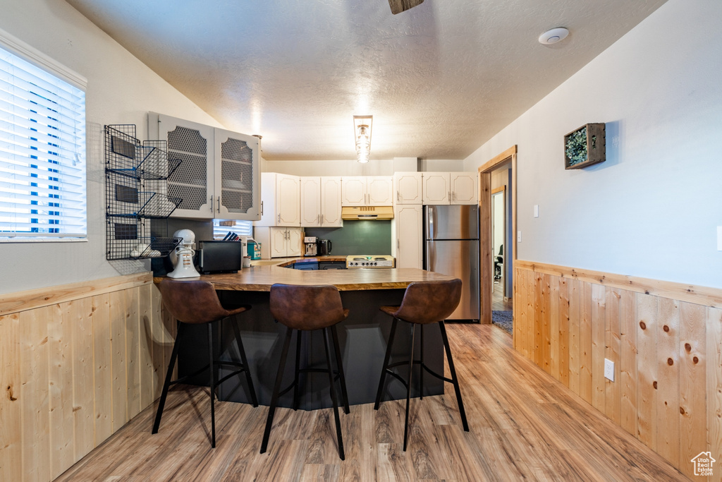 Kitchen with stainless steel fridge, light wood-type flooring, white cabinetry, kitchen peninsula, and a breakfast bar area