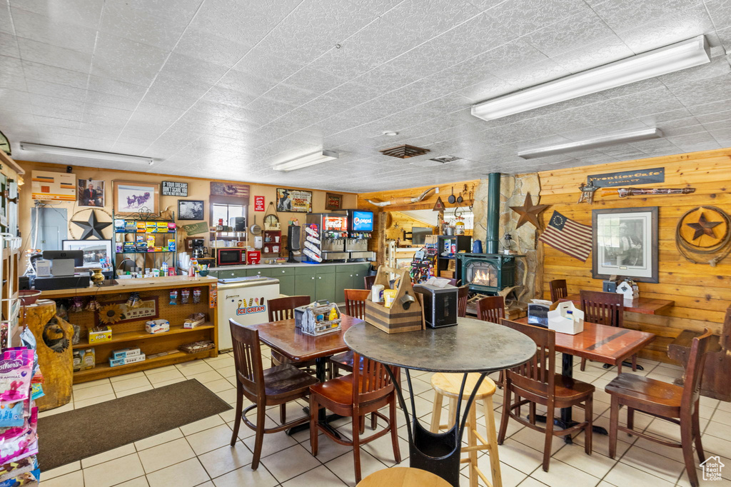 Dining area featuring a workshop area, light tile patterned floors, a wood stove, and wooden walls