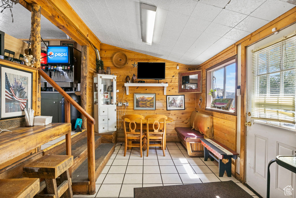 Dining room with light tile patterned floors, lofted ceiling, and wood walls