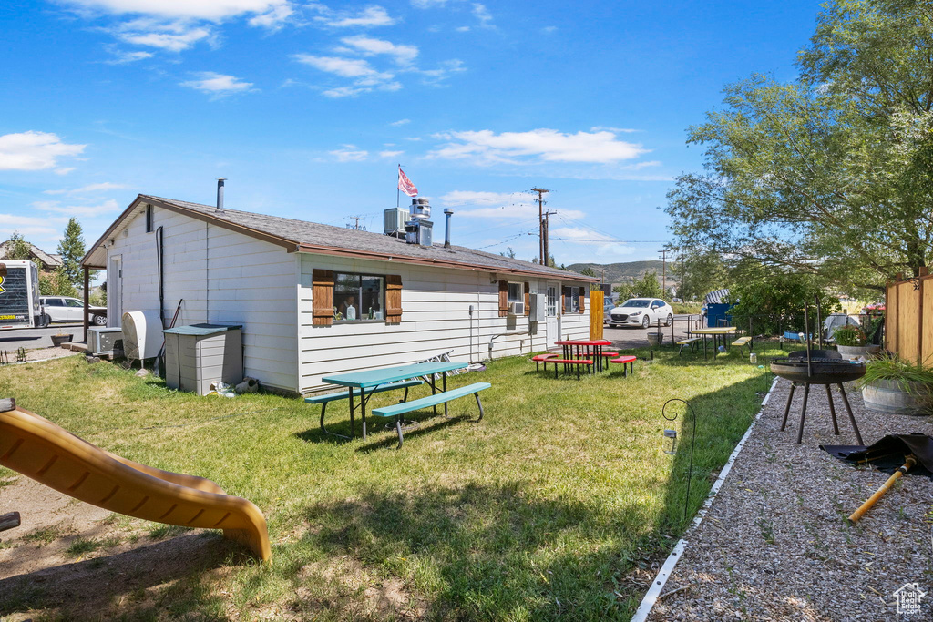 Rear view of house with cooling unit, a playground, and a yard