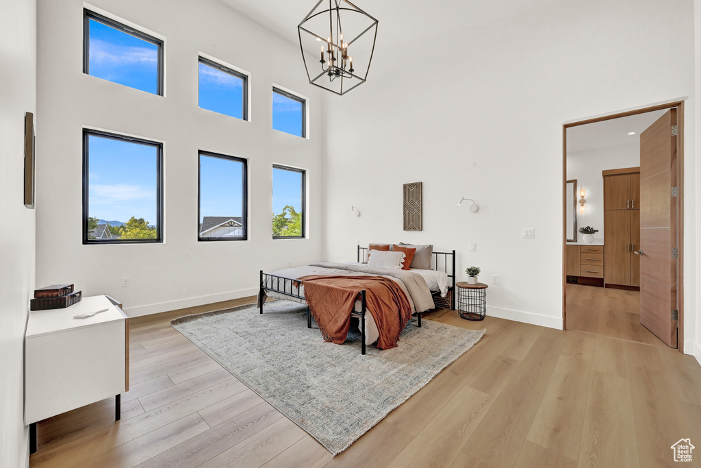 Bedroom with light wood-type flooring, an inviting chandelier, and a towering ceiling