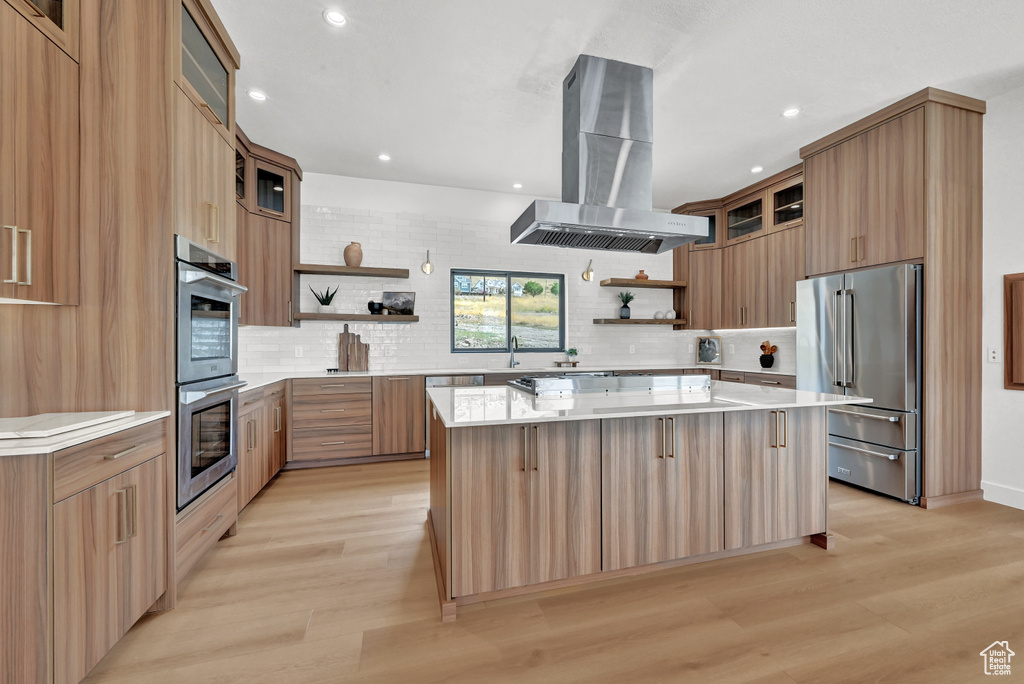 Kitchen featuring light hardwood / wood-style flooring, island range hood, stainless steel appliances, a spacious island, and decorative backsplash