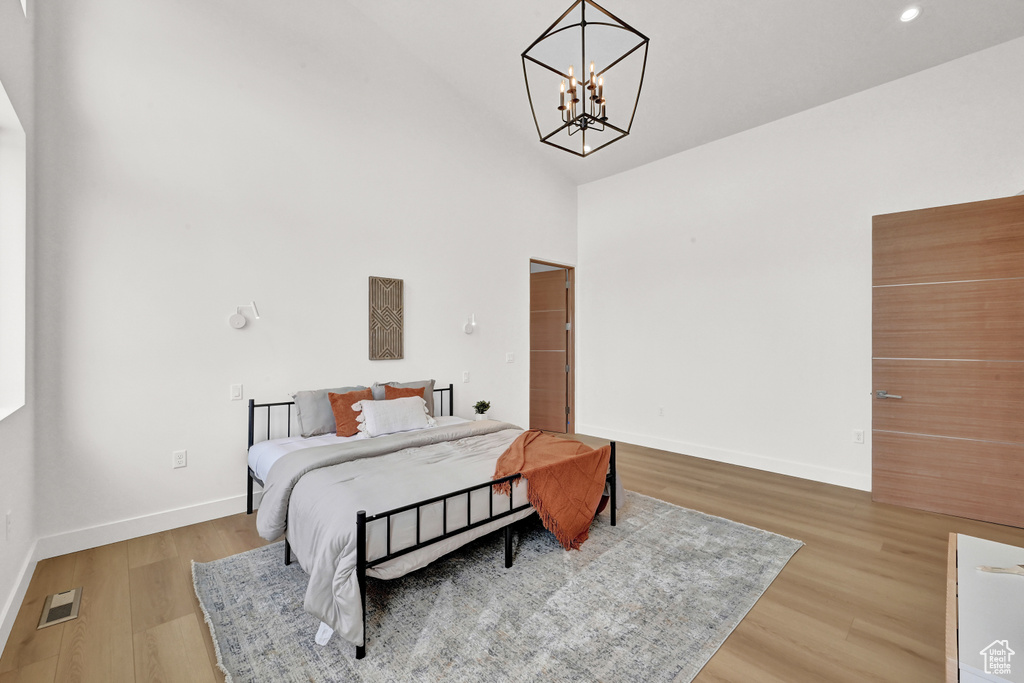 Bedroom featuring an inviting chandelier, high vaulted ceiling, and wood-type flooring