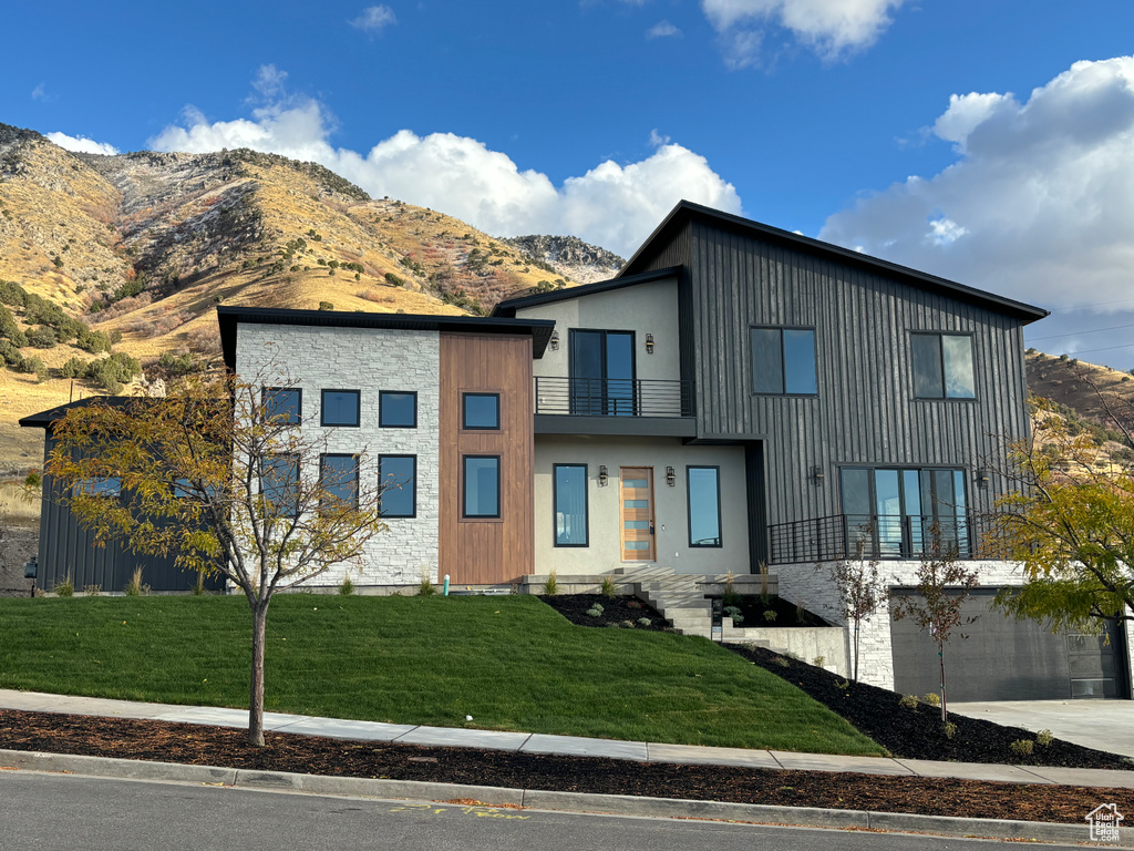 Modern home with a balcony, a front lawn, and a mountain view