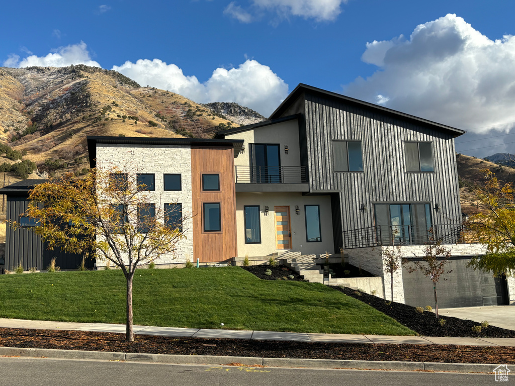 Modern home with a front yard, a balcony, and a mountain view