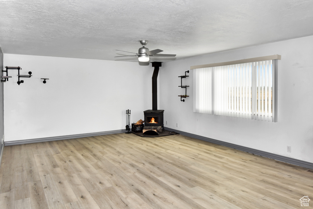 Unfurnished living room featuring a textured ceiling, ceiling fan, a wood stove, and light wood-type flooring