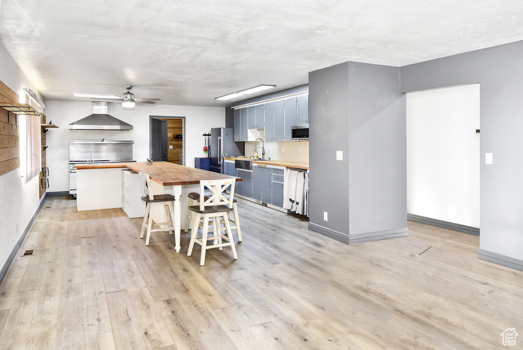 Kitchen with a breakfast bar area, stainless steel appliances, wood counters, sink, and wall chimney range hood