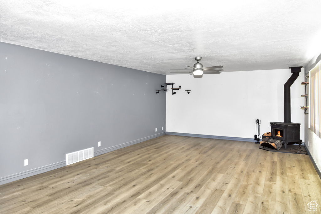 Unfurnished living room featuring a textured ceiling, ceiling fan, light hardwood / wood-style flooring, and a wood stove