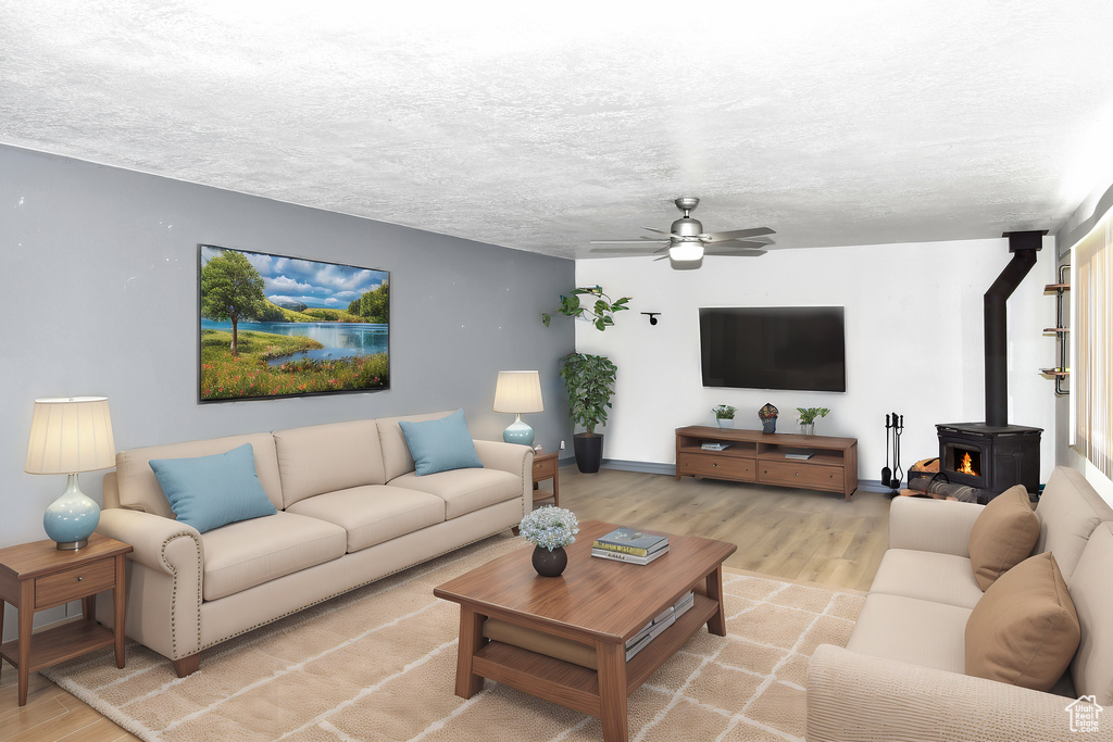Living room with a textured ceiling, ceiling fan, light hardwood / wood-style floors, and a wood stove