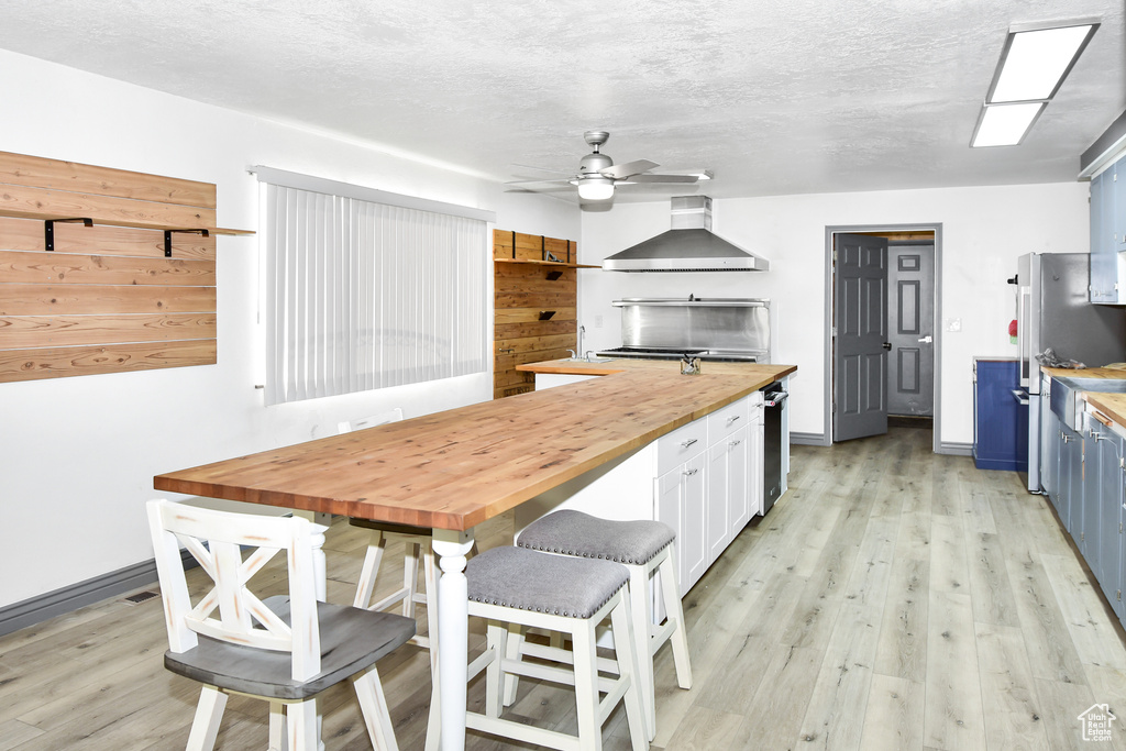 Kitchen with wall chimney range hood, wood counters, white cabinetry, blue cabinets, and ceiling fan