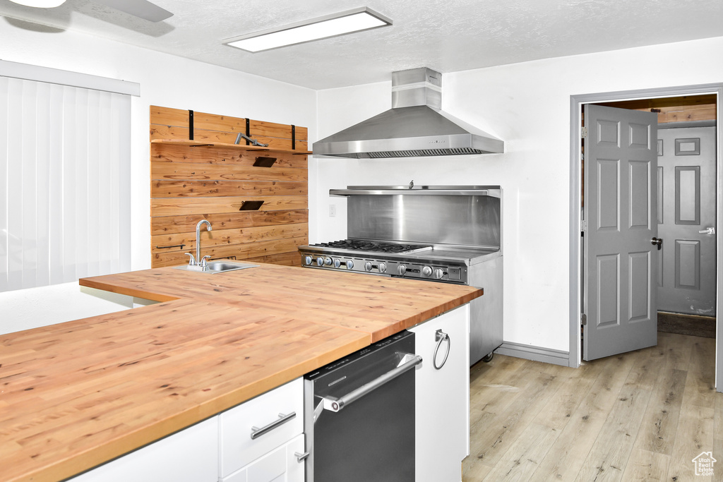 Kitchen with sink, wooden walls, a textured ceiling, white cabinets, and wall chimney range hood