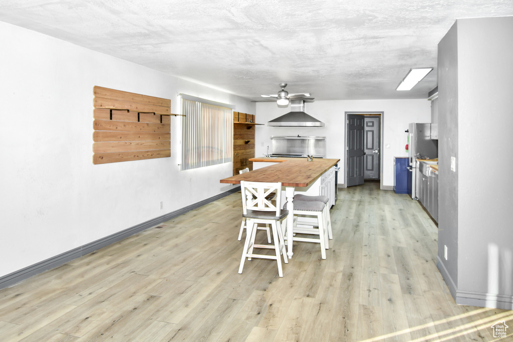 Kitchen with wall chimney exhaust hood, a breakfast bar, wooden counters, light wood-type flooring, and ceiling fan