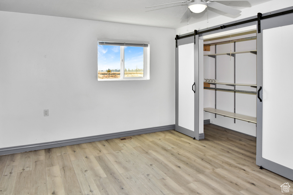 Unfurnished bedroom with ceiling fan, a barn door, and light hardwood / wood-style floors