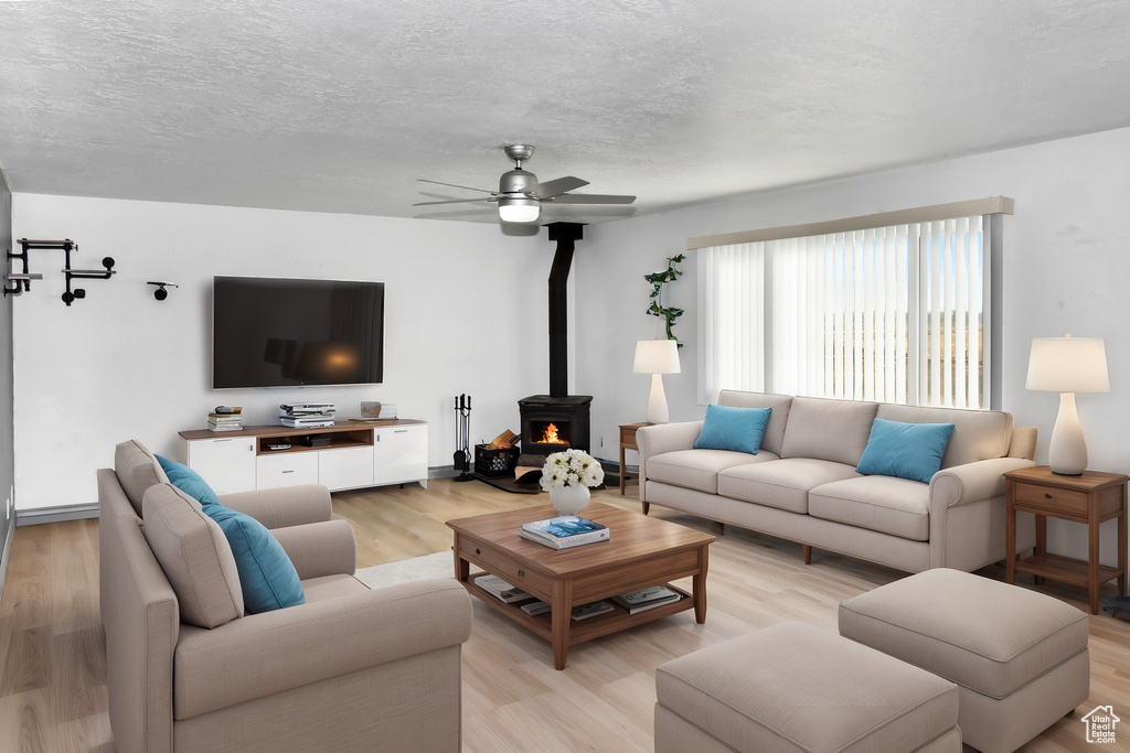 Living room with light wood-type flooring, ceiling fan, a textured ceiling, and a wood stove