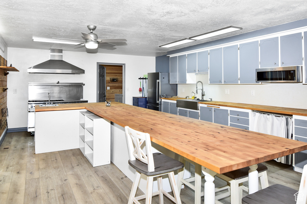 Kitchen featuring wall chimney range hood, wood counters, blue cabinets, appliances with stainless steel finishes, and sink
