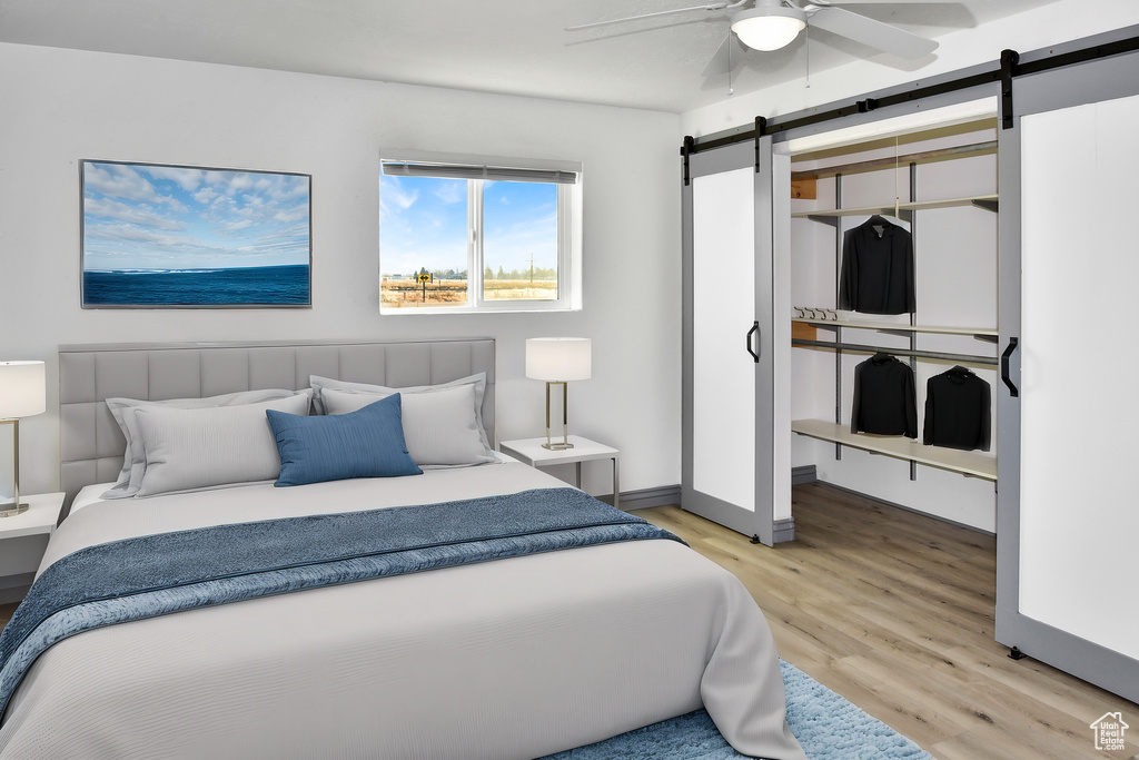 Bedroom featuring ceiling fan, light hardwood / wood-style floors, and a barn door