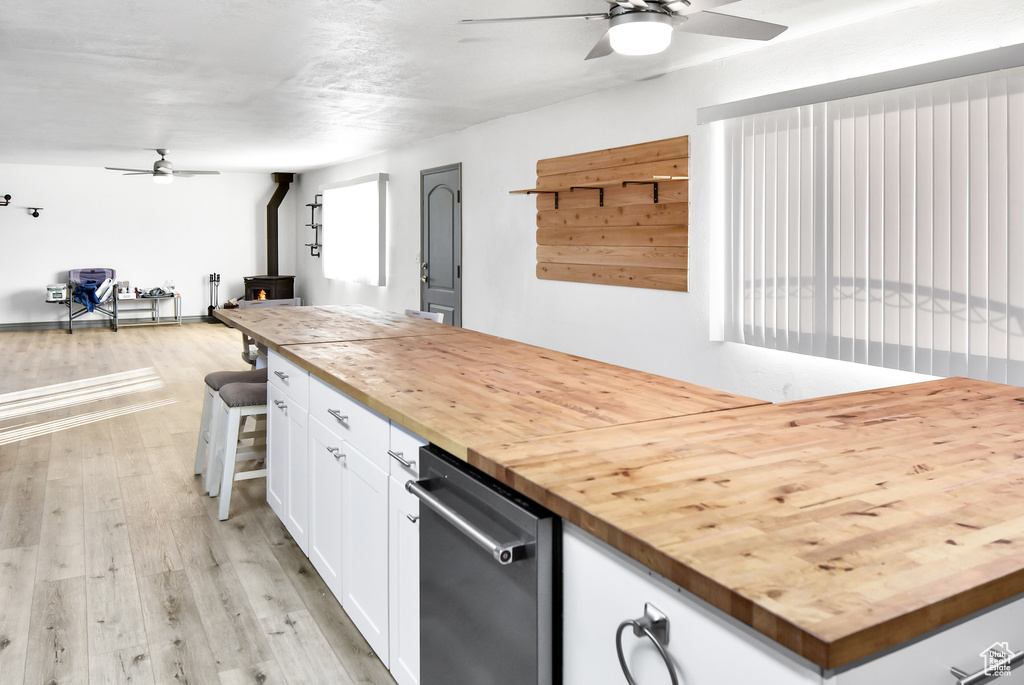 Kitchen with white cabinetry, butcher block countertops, light wood-type flooring, and a wood stove