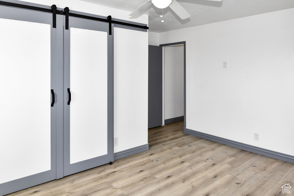 Unfurnished room with ceiling fan, a barn door, and light hardwood / wood-style floors