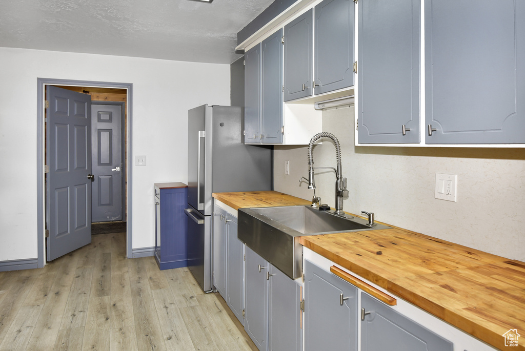 Kitchen featuring sink, stainless steel fridge, light hardwood / wood-style flooring, and butcher block counters