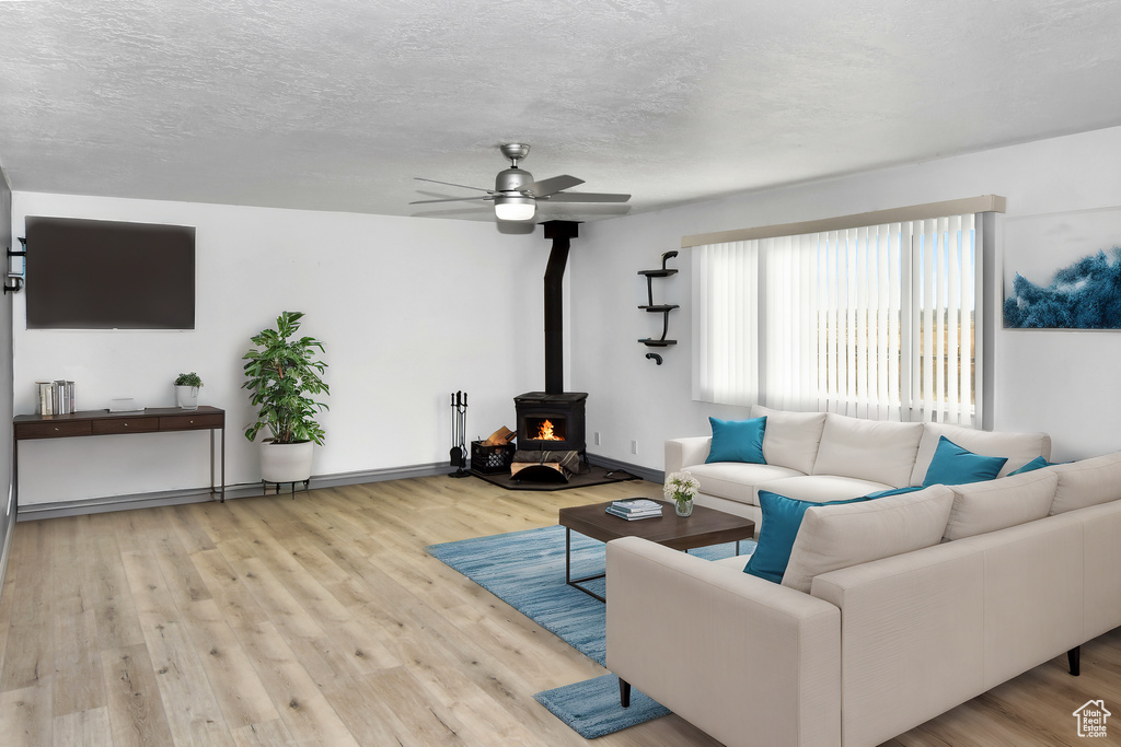 Living room featuring a textured ceiling, ceiling fan, light hardwood / wood-style flooring, and a wood stove