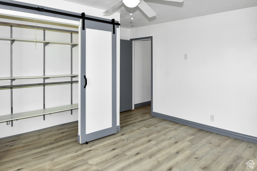 Unfurnished bedroom featuring a closet, ceiling fan, hardwood / wood-style flooring, and a barn door