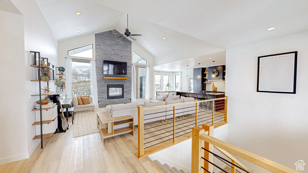 Living room with high vaulted ceiling, light wood-type flooring, ceiling fan, and a stone fireplace