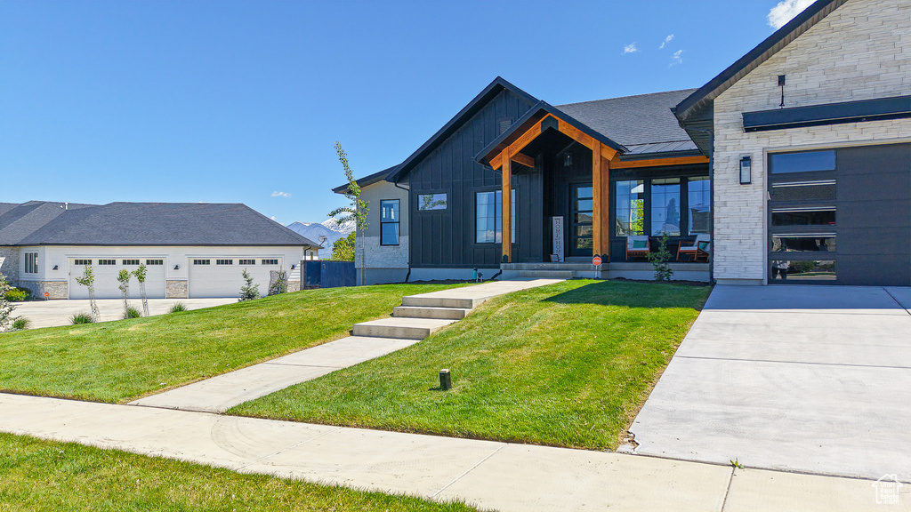 View of front of home featuring a front yard, covered porch, stone siding, board and batten siding, and a garage